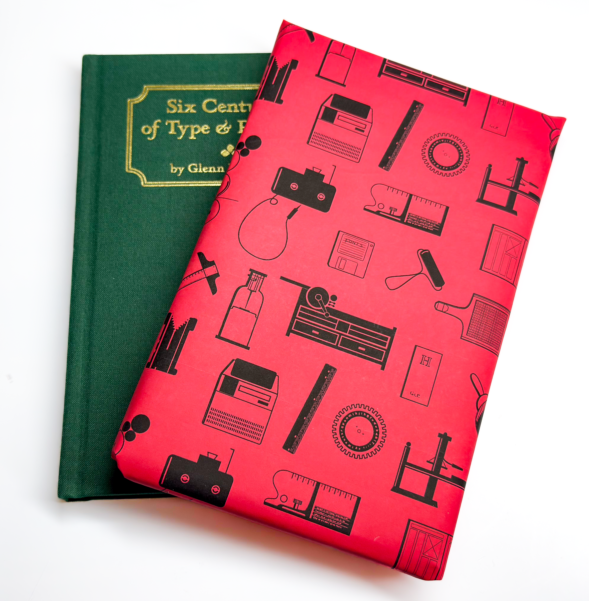 Gift wrapped copy wrapped in red paper with typography artifact pattern lying on top and askew an unwrapped copy of the book